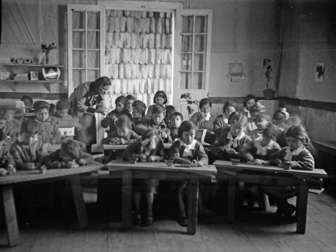 Fotografía: Niñas, niños y profesora en sala de clases de Escuela Anexa a la Normal, ca. 1940. Fondo Enrique Caro B., Colección Museo Regional de Ancud.