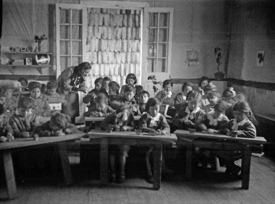 Fotografía: Niñas, niños y profesora en sala de clases de Escuela Anexa a la Normal, ca. 1940. Fondo Enrique Caro B., Colección Museo Regional de Ancud.